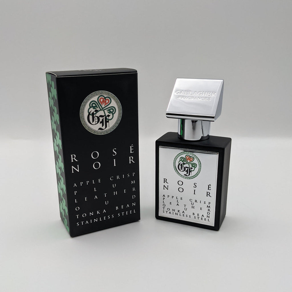 A bottle of Gallagher Fragrances Rose Noir perfume stands next to its box. The black bottle with a silver cap exudes elegance. The box features the same design and lists fragrance notes like apple crisp, leather, and a hint of Turkish Rose Absolute.