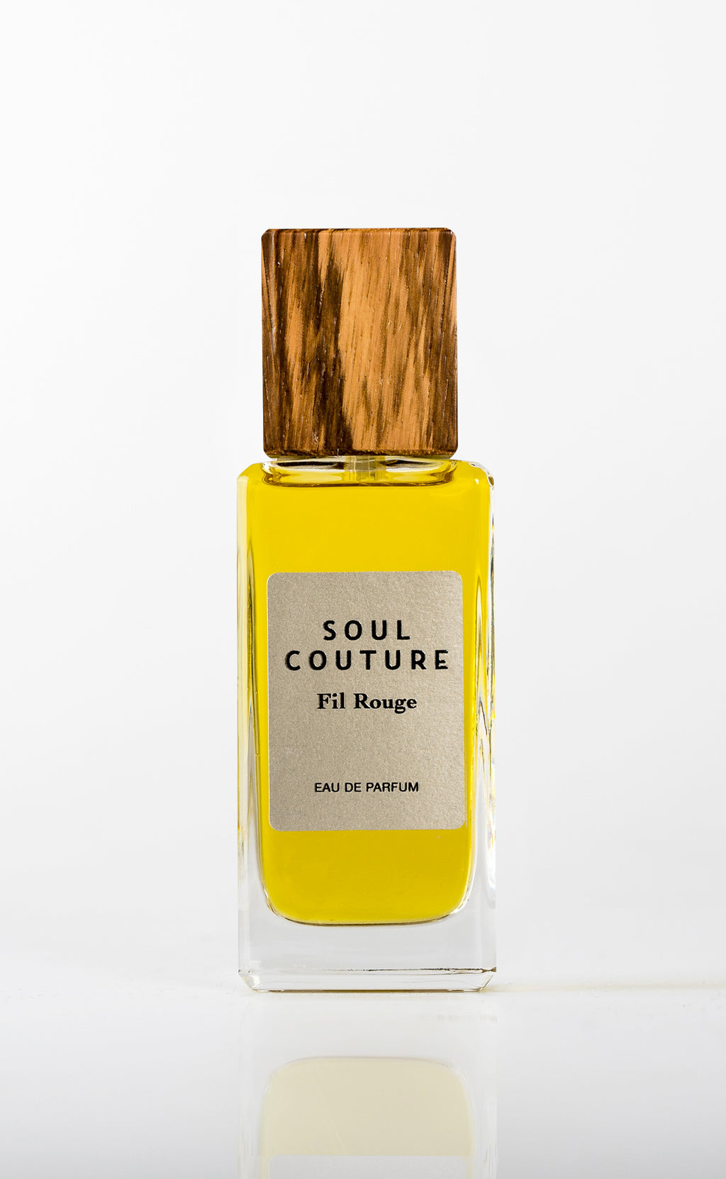A bottle of Soul Couture Fil Rouge Eau de Parfum, infused with noble essences, features yellow liquid and a wooden cap.