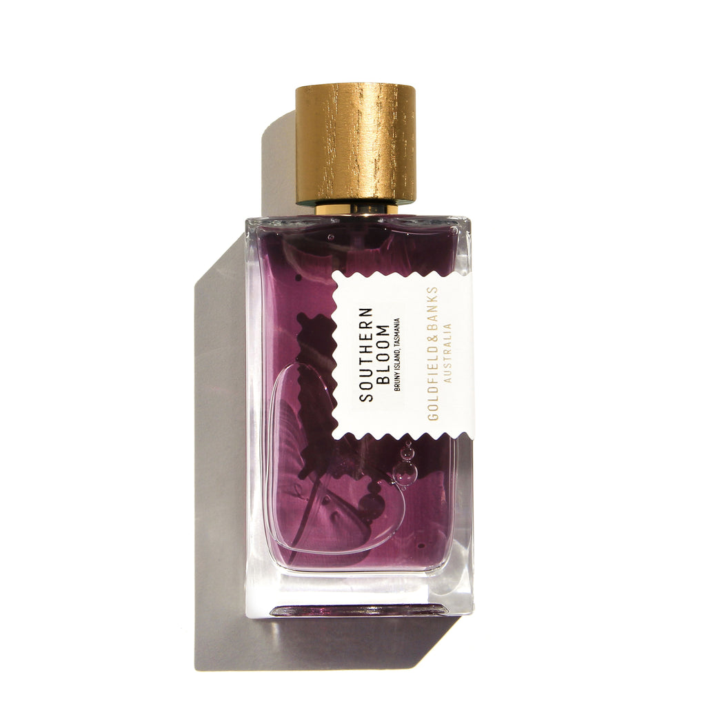 A bottle of Southern Bloom by Goldfield & Banks features a gold cap and purple liquid inside, embodying the luxurious fragrance of Boronia Absolute. The label is white with text details in black and gold.
