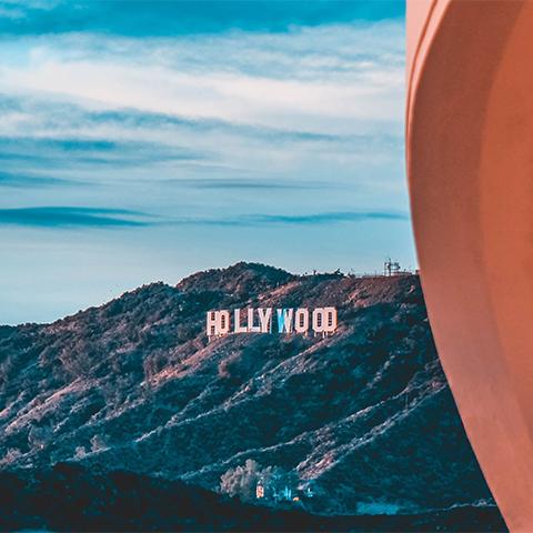 The Hollywood sign is displayed on a hillside under a blue sky, next to the edge of a curved structure in the foreground, with a hint of Los Angeles by Gallivant wafting through the air.