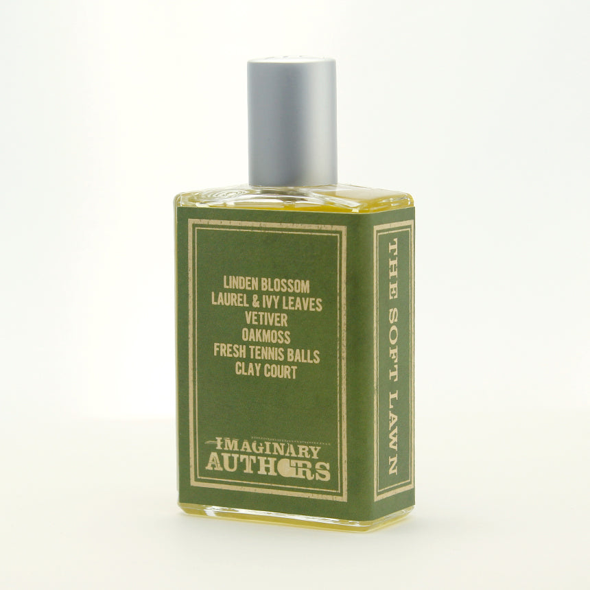 A green bottle of "The Soft Lawn" by Imaginary Authors with a silver cap and a label listing ingredients like linden blossom, vetiver, and oakmoss, evoking the nostalgic charm of a sun-lit tennis court.