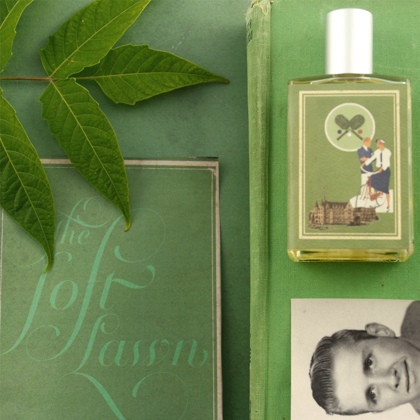 Green-themed flatlay featuring a perfume bottle with a vintage illustration of Linden Blossom, green books, and green leaves. A black-and-white photo of a man's face appears in the corner. The Soft Lawn by Imaginary Authors sits prominently among the items.