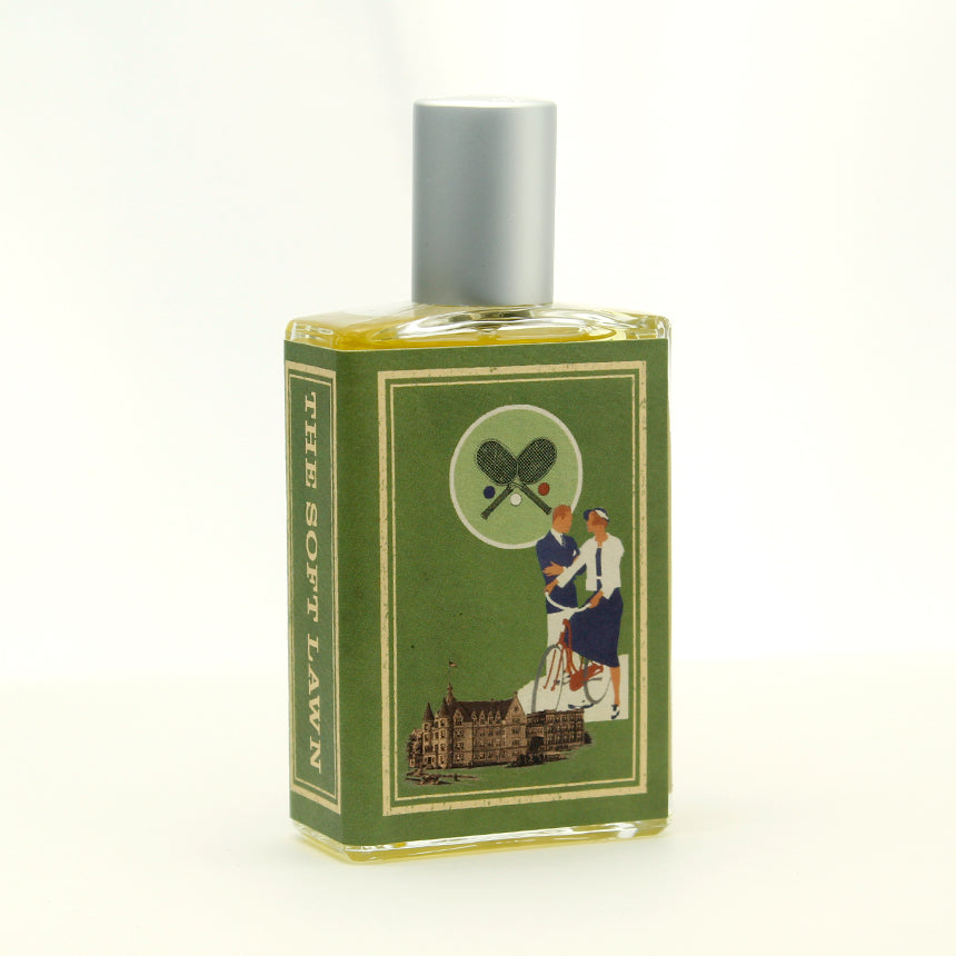 A bottle of "The Soft Lawn" by Imaginary Authors with a green label featuring an illustration of two people in tennis attire, a historic building, and a backdrop reminiscent of an elegant tennis court. The scent captures delicate notes of linden blossom and vetiver.
