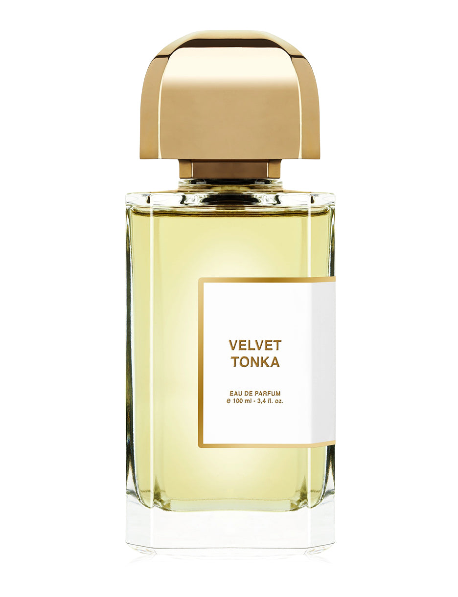 A clear glass perfume bottle from BDK Parfums with a gold cap, labeled "Velvet Tonka Eau de Parfum 100 ml 3.4 fl. oz." containing light yellow liquid infused with the warm essence of Tonka bean and delicate notes of orange blossom.
