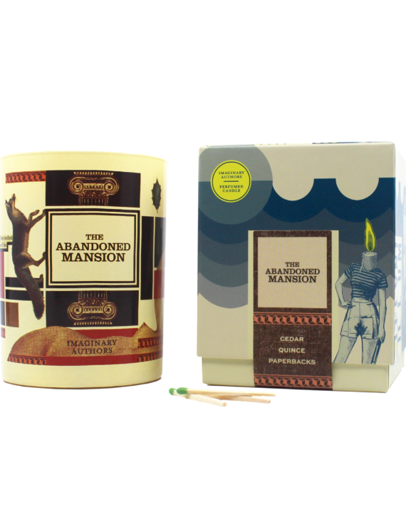 A candle named "The Abandoned Mansion" by Imaginary Authors stands beside its packaging, which showcases the scent of cedar and quince, with two matchsticks placed in front.