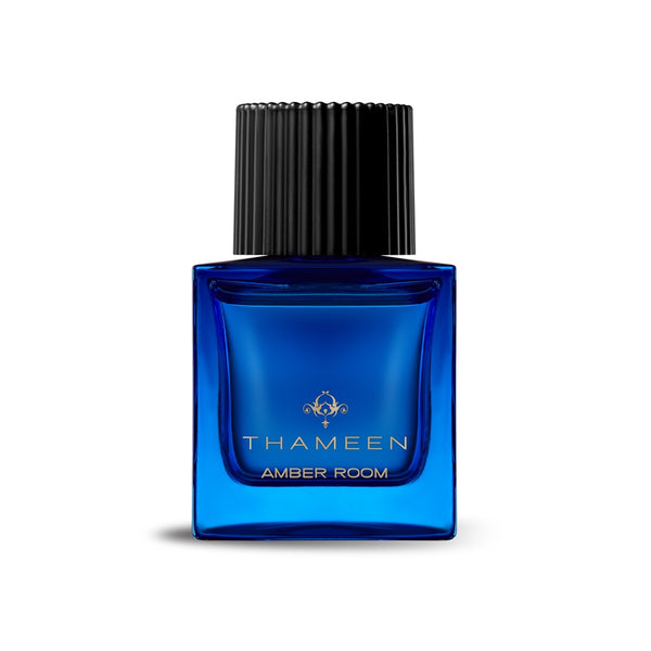 A blue glass bottle of THAMEEN Amber Room perfume with a hint of Bulgarian rose, featuring a black ribbed cap and a gold logo on the front.