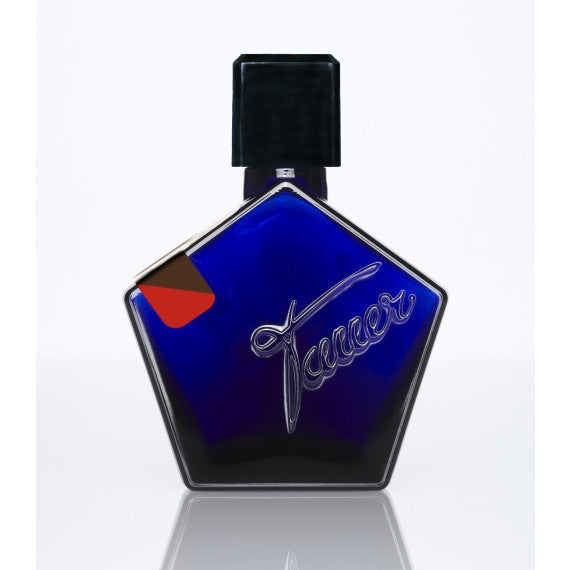 A blue pentagon-shaped perfume bottle with a black cap and cursive script detail, reflecting on a white surface, encapsulating the essence of Au Coeur Du Desert by Tauer Perfumes.