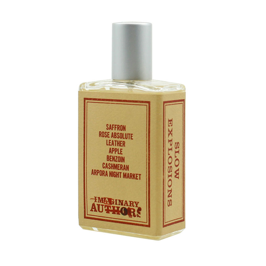 A rectangular perfume bottle labeled "Slow Explosions" by Imaginary Authors. The label lists its notes: saffron, rose absolute, leather, apple, benzoin, cashmeran, and Arpora Night Market.