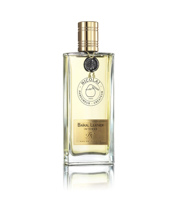 A clear glass bottle of Nicolaï's Baïkal Leather eau de parfum with a gold cap and label, containing light yellow liquid with hints of spicy citrus and woody notes.