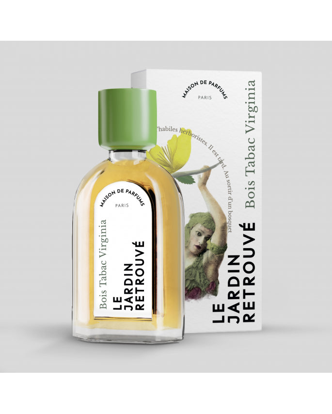 A bottle of Le Jardin Retrouvé Bois Tabac Virginia stands in front of its matching box. The box features artwork of a woman and a green leaf, perfectly complementing the smoked vetiver notes within the fragrance.