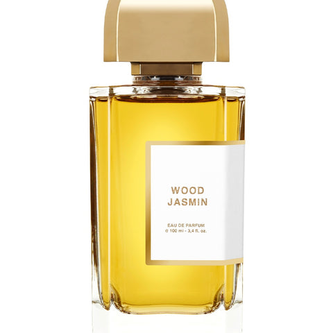 A clear glass bottle of Wood Jasmin Eau de Parfum by BDK Parfums with a gold cap, containing a golden liquid. The white label shows the perfume name and volume details. This precious elixir combines the essence of jasmine with the allure of mysterious woods.
