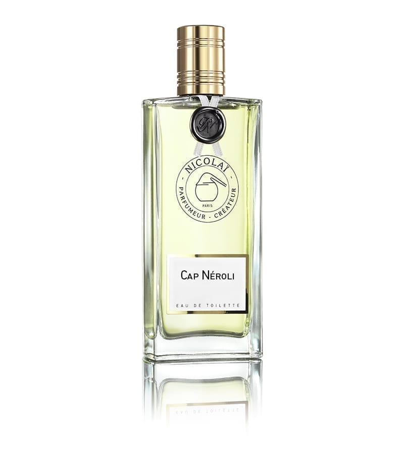 A clear glass bottle of Nicolaï Cap Neroli Eau de Toilette with a gold cap, a logo, and a white label on the front, exuding the vibrant essence of bitter orange.