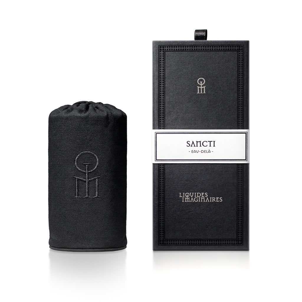 A cylindrical black perfume bottle sits beside a rectangular black box, both labeled "Sancti" by "Liquides Imaginaires," and exude an aura of spiritual elevation with their woodsy incense fragrance.