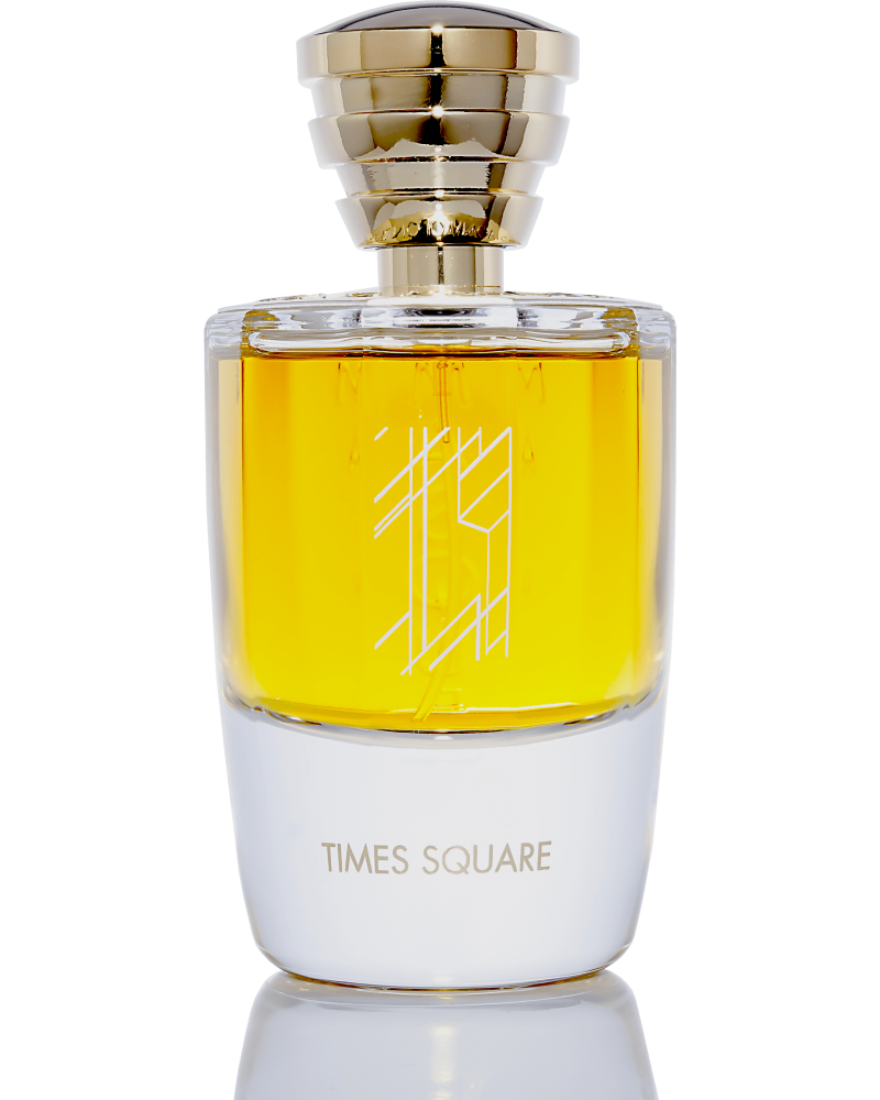 A clear glass bottle of Masque Milano's Times Square perfume containing golden liquid, adorned with a golden cap and a geometric design on the front. This elegant fragrance captures the essence of New York's vibrant city miasmas.