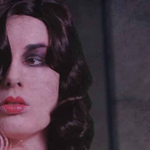 Close-up of a person with long dark hair, heavy makeup featuring dark eyeshadow and bright red lipstick from Ikiryo's Coralie collection, reminiscent of a character from a 1929 murder mystery. They are looking slightly off to the side.