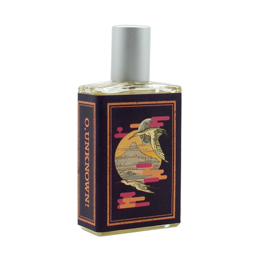 A rectangular perfume bottle with a silver cap features a purple label showcasing a stylized bird flying over a sunset with a mountain in the background and the words "O, Unknown!" in gold, hinting at the enticing scents of sandalwood and musk balsam within by Imaginary Authors.