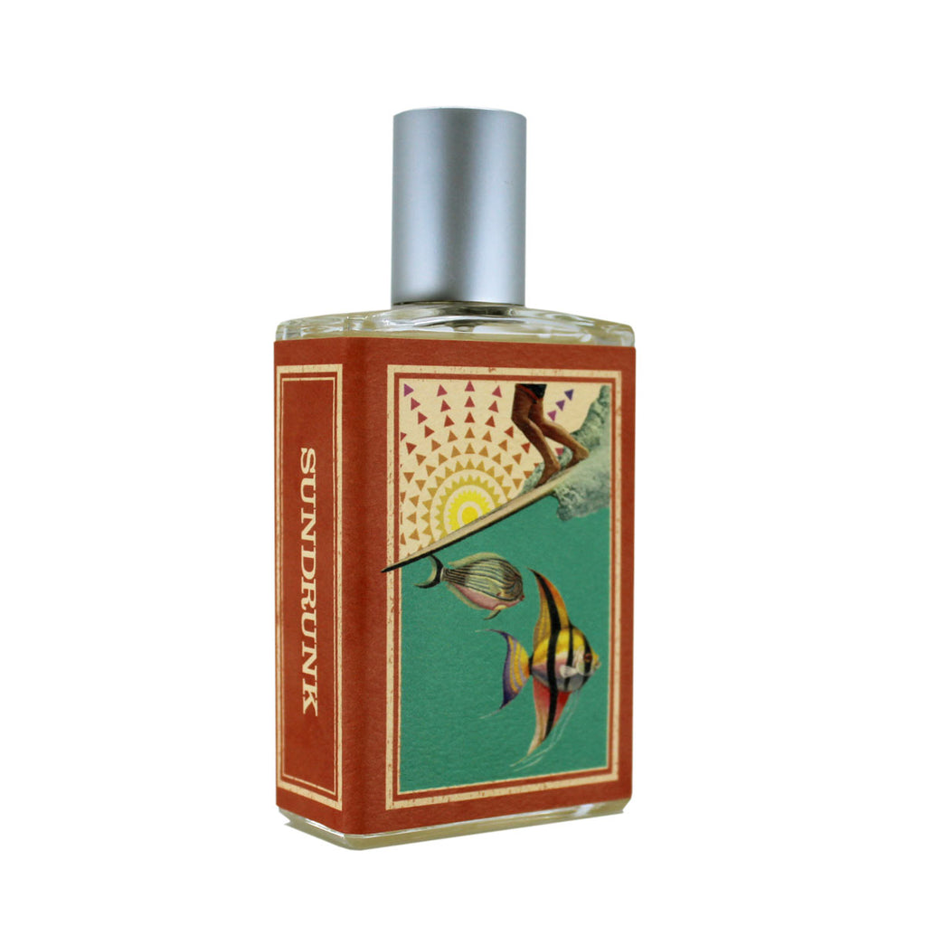 The "Sundrunk" rectangular perfume bottle from Imaginary Authors showcases a vibrant design featuring fish and a sun on a red background, alluding to notes of honeysuckle. It is topped with a silver cap.
