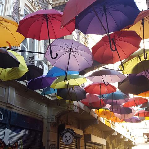 Colorful umbrellas hang suspended over a narrow street in the ancient city, creating a lively canopy above pedestrians, all while the enchanting scent of Istanbul by Gallivant from Gallivant Perfumes fills the air with notes of bergamot.