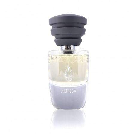 A glass bottle of Masque Milano's L'Attesa perfume features a clear upper half containing yellow liquid, paired with a solid grey bottom half. Encased by a black cap with multiple ridges, the scent evokes the aroma of freshly plucked flowers on a summer night.