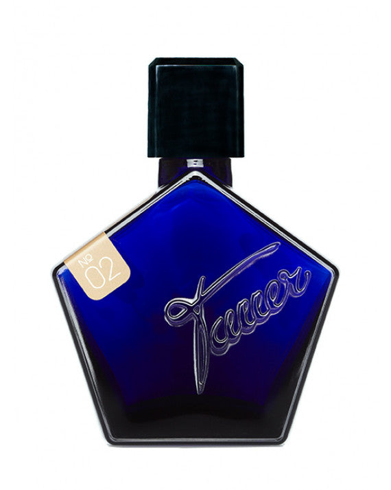 A cobalt blue, pentagon-shaped perfume bottle with a black cap and a label marked "No. 02 L'Air Du Desert Marocain" on the top left corner. The bottle, evoking a Moroccan night, has the word "Tauer Perfumes" engraved on the front.