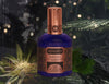 A bottle of House of Matriarch Black No. 1 (Blackbird) men's fragrance sits against a forest-themed background, surrounded by green foliage. The dark blue bottle, adorned with copper-colored geometric designs, exudes exotic natural essences.