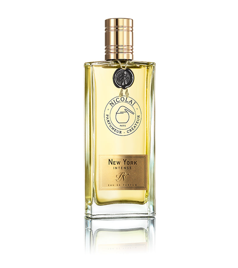 A bottle of New York Intense by Nicolaï, adorned with a gold cap and label, filled with a light amber liquid that radiates an enchanting spicy fragrance.