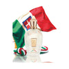 A bottle of Xerjoff Renaissance perfume with a beige cap is placed in front of a red, white, and green flag. The bottle has a gold embossed label and a braided cord in similar flag colors beside it, evoking the fresh essence of Italian citrus.