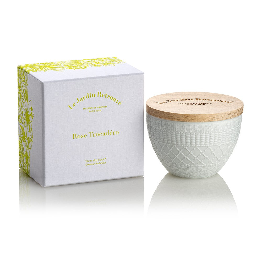 A white ceramic candle with a wooden lid is placed next to its box, labeled "Rose Trocadéro" by Le Jardin Retrouvé, featuring a yellow floral design reminiscent of classic French perfumes.
