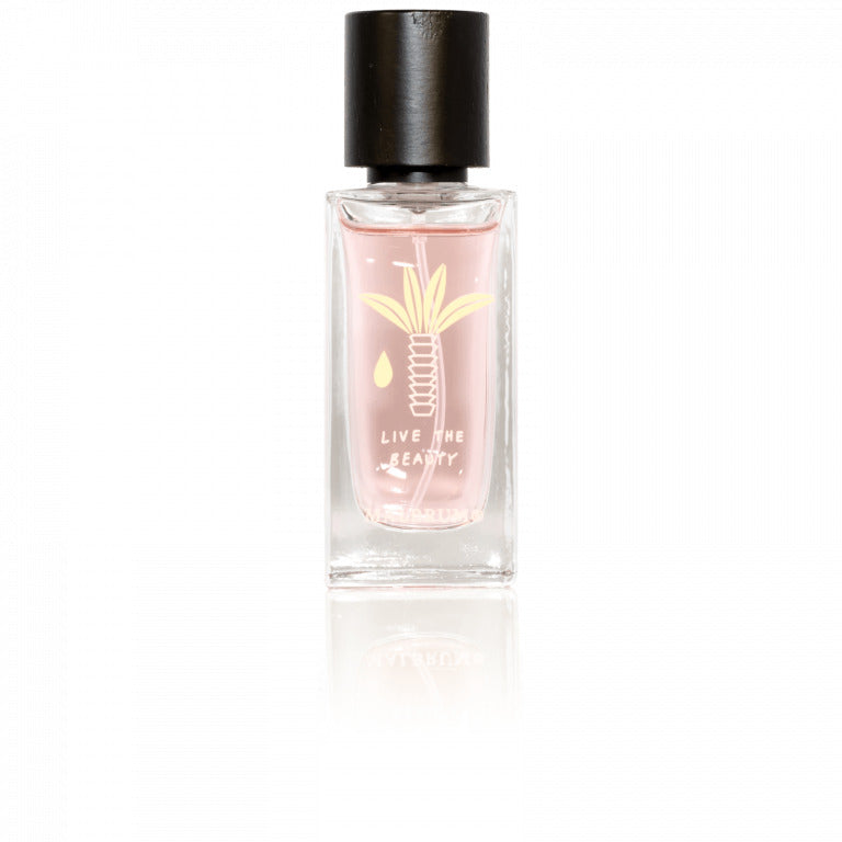 The clear glass bottle with a black cap contains a pink liquid, exuding tropical fruity notes. The bottle features a logo with a stylized plant and the words "LIVE THE BEAUTY" printed on it, and is named Safariyah by Malbrum Parfums.