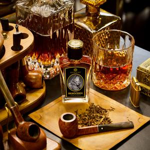 A bottle of Bemboka whiskey, a filled whiskey glass, Red Earth Tobacco, and pipes are arranged on a table. Decanters and a box are also visible in the background, enhancing the sophisticated scent of Rhinoceros by Zoologist that permeates the room.