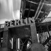 A black and white photo captures a large concrete sign reading "Berlin" mounted under a metal bridge structure, evoking the bold essence of Berlin by Gallivant from Gallivant Perfumes.
