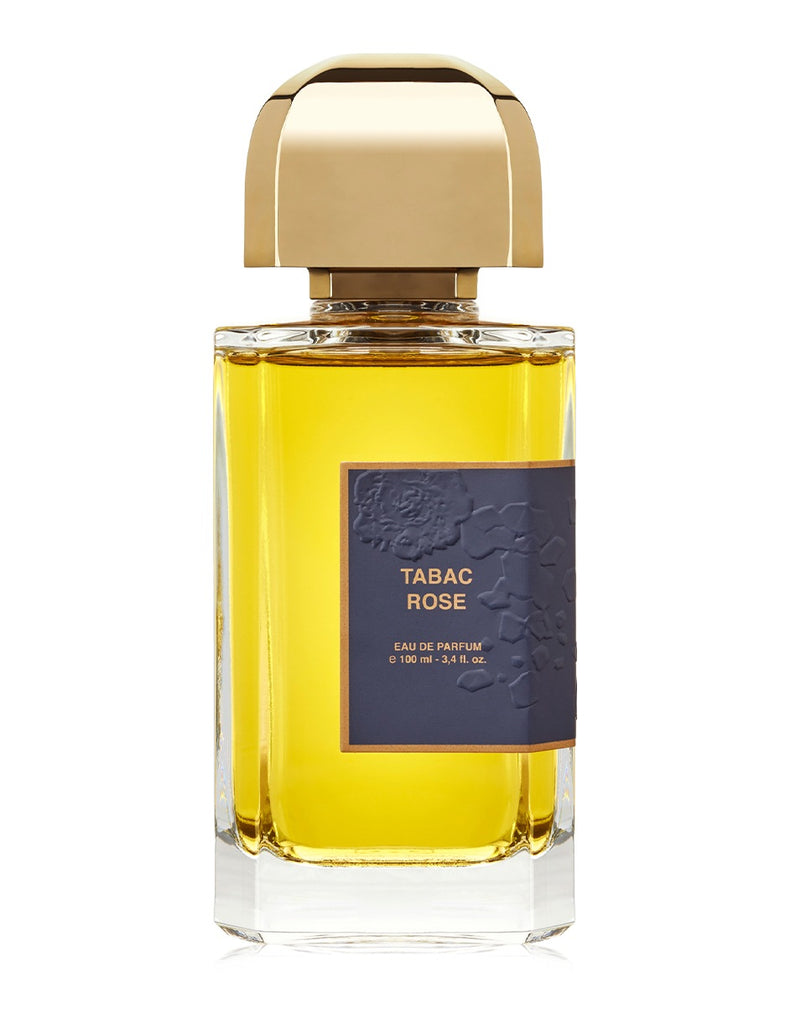 A bottle of "Tabac Rose" Eau de Parfum by BDK Parfums, 100 ml in size, is adorned with a dark label bearing raised floral detail and crowned with a gold cap. It contains a golden liquid that perfectly captures the essence of Turkish rose and opulent tobacco.